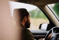 一名戴着无檐帽、留着胡子的男子驾驶着一辆背景模糊的汽车