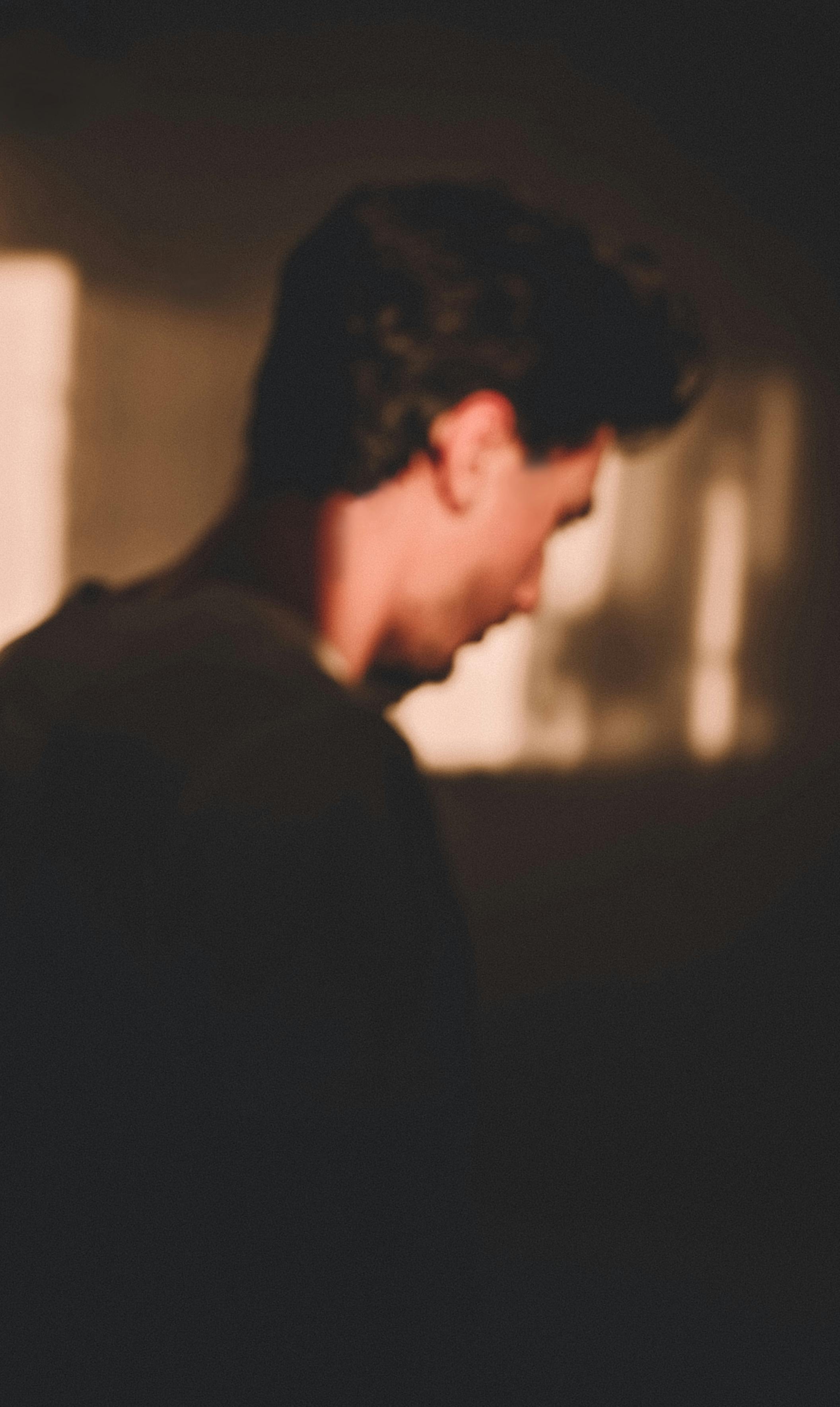 Side view of defocused young man standing in room at sunlight and looking down