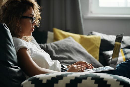 Woman with glasses comfortably working at home on her laptop during daylight.