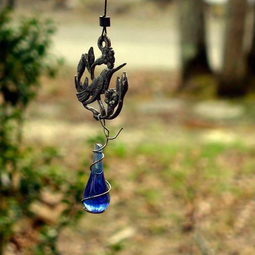 Free Metal decoration in shape of bird with ornament and bright blue crystal hanging on street against forest Stock Photo