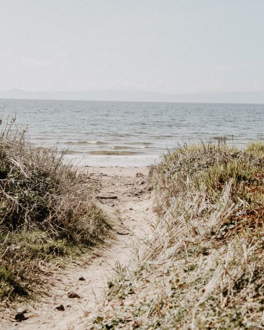 Tranquil sandy path leading to the ocean at Portencross, Scotland, under a clear sky.