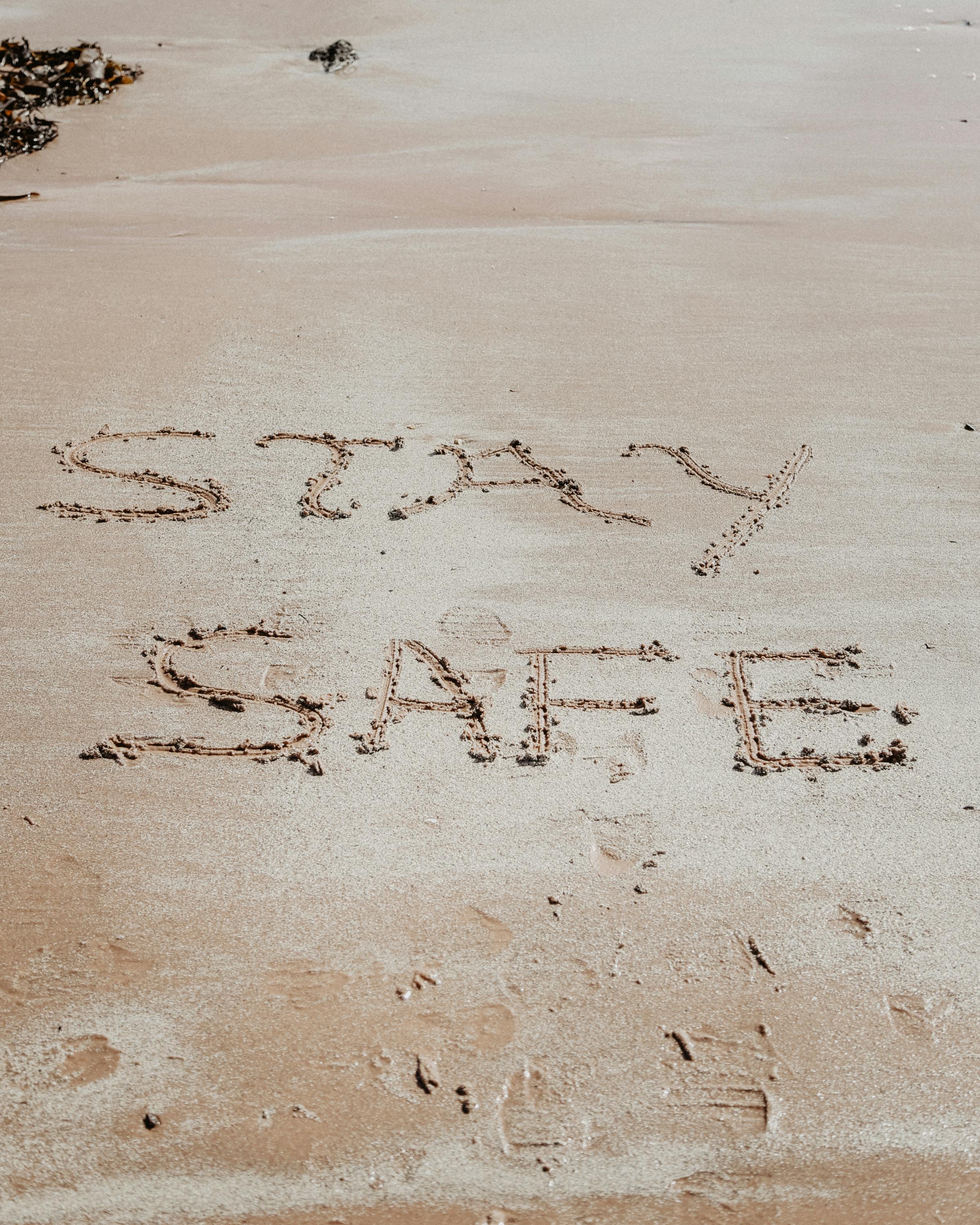 Stay safe message inscribed on sandy shore at Portencross Beach, Scotland, conveying warmth and caution.