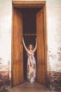 Woman in White and Red Floral Dress Standing in Front of Brown Wooden Door