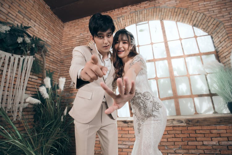 Happy Asian Bride And Groom Pointing At Camera