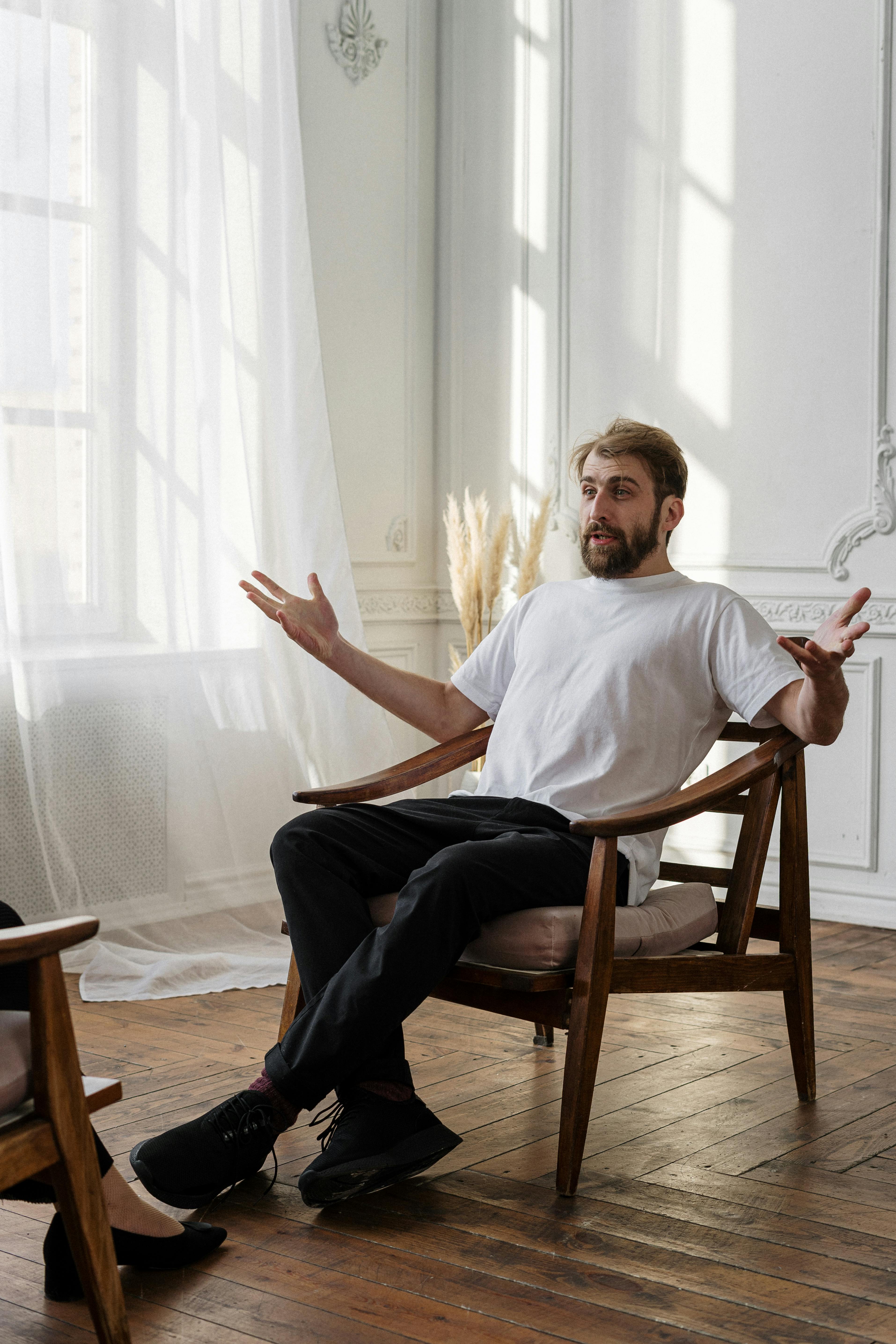 man in white crew neck t shirt sitting on brown wooden rocking chair