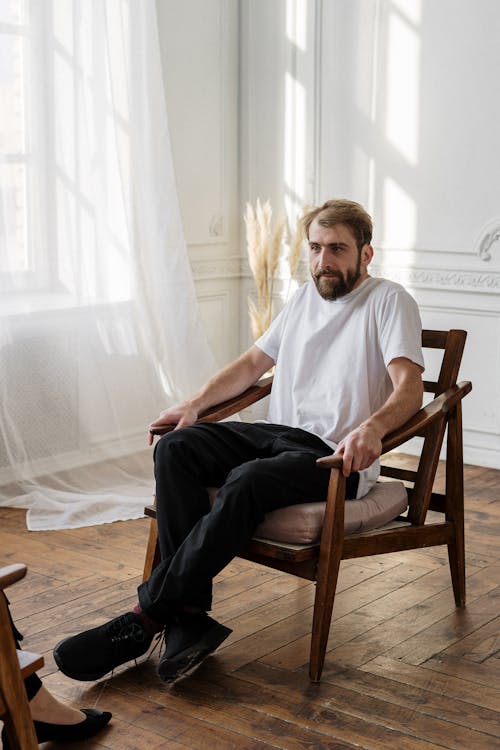 Man in White Crew Neck T-shirt Sitting on Brown Wooden Armchair