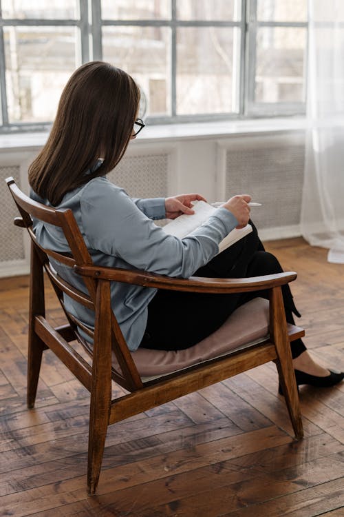 Free Woman in White Long Sleeve Shirt Sitting on Brown Wooden Chair Stock Photo