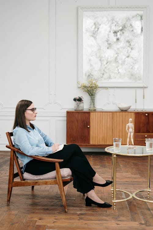 Woman in Blue Dress Shirt Sitting on Brown Wooden Chair