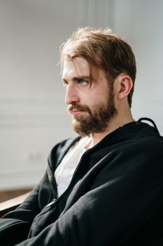 一个留着胡子的男人坐在室内，沐浴在柔和的阳光下，神情深思熟虑