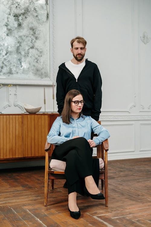 Man in Black Jacket Sitting on Brown Wooden Chair Beside Woman in Gray Long Sleeve Shirt