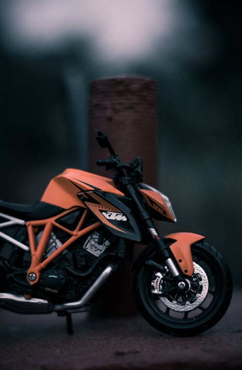 Closeup of small black orange motorcycle with black wheels next to metal pillar on blurred background