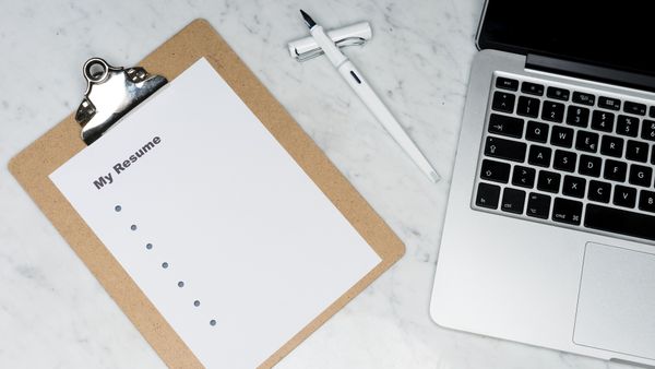 A clipboard with a resume beside a pen and laptop on a desk