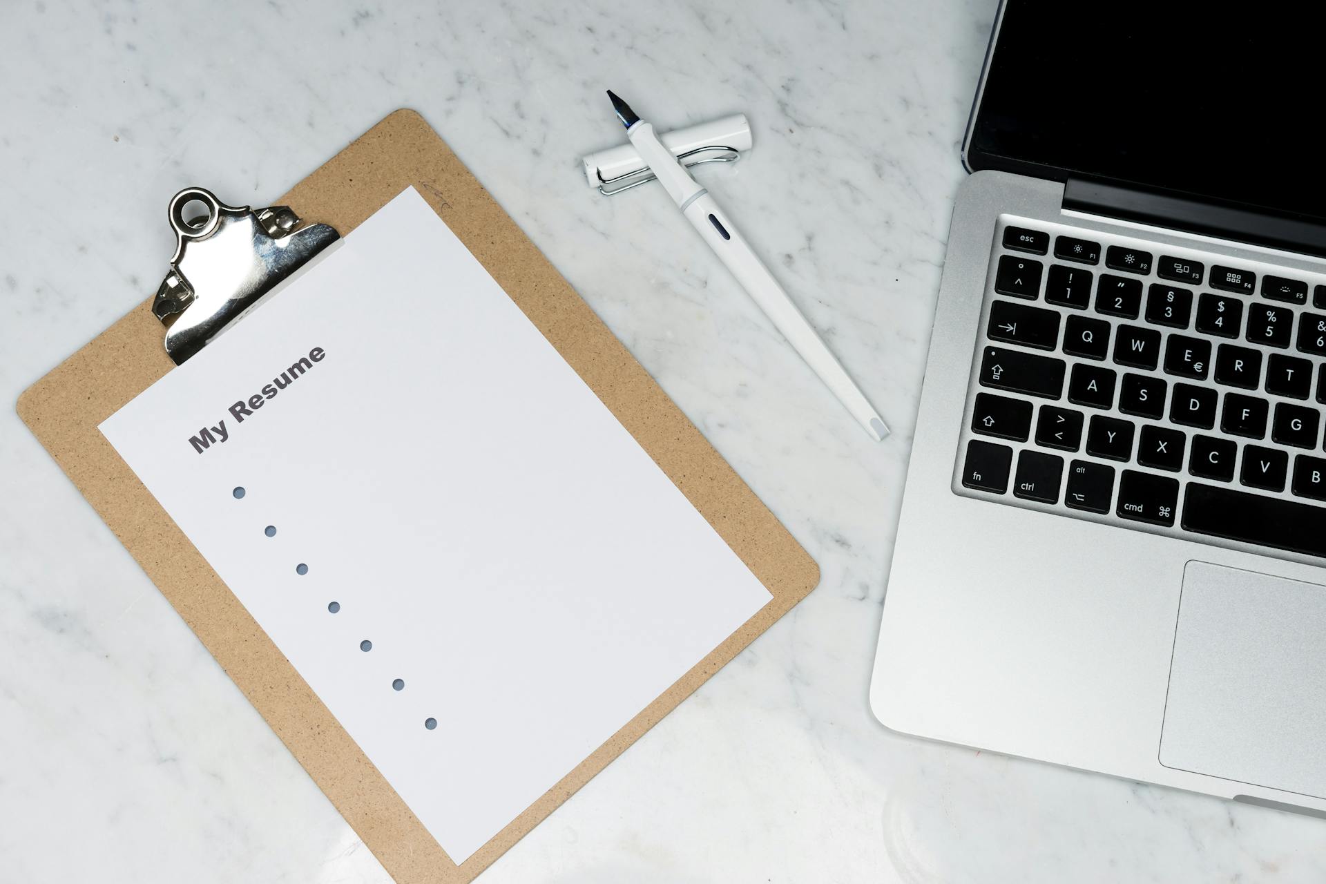 A clipboard with a resume beside a pen and laptop on a marble desk, ideal for business and job application themes.