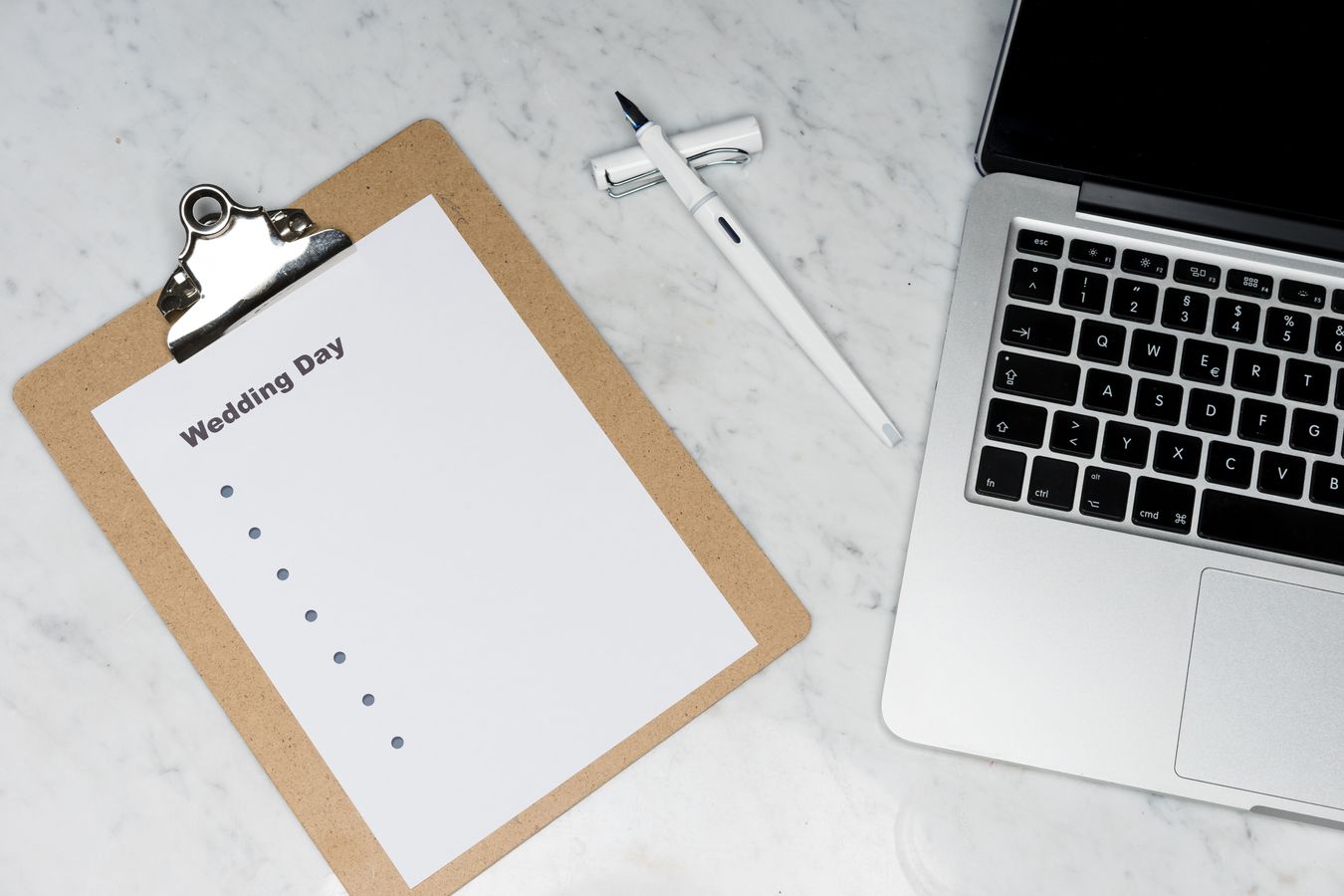 Portapapeles con lista de pendientes de boda junto a una laptop sobre un escritorio
