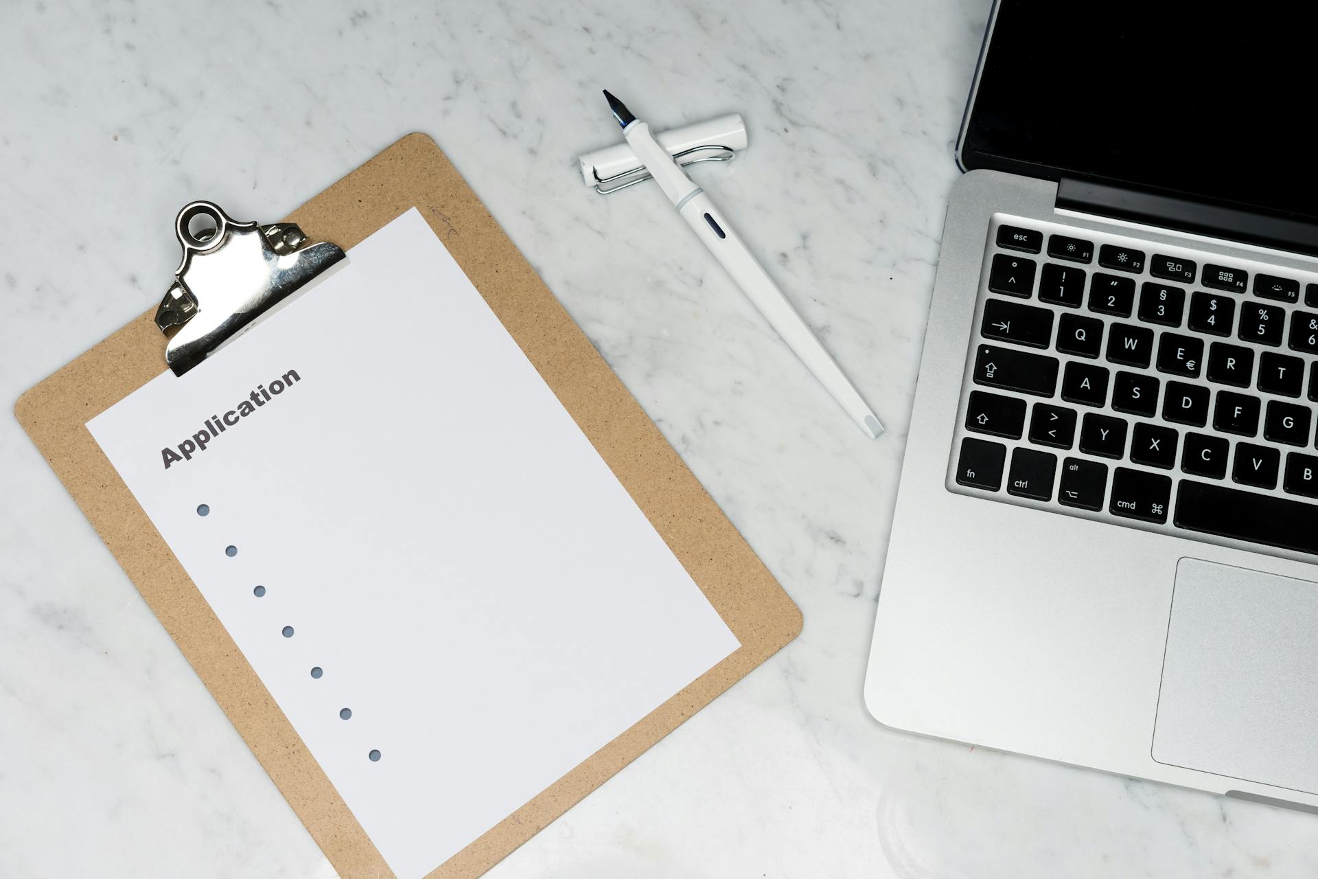 A clean and organized office desk setup featuring a laptop, clipboard with application form, and pen.