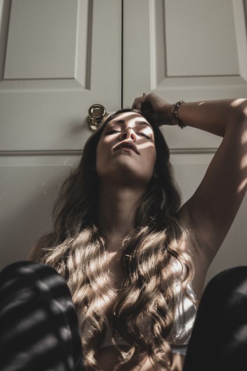 Free Artistic portrait of woman sitting indoors with dramatic light and shadow pattern. Stock Photo