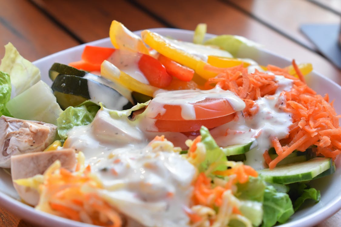 Free Salad of fresh grated carrots and cut tomato with lettuce and slices of hum covered with white dressing Stock Photo