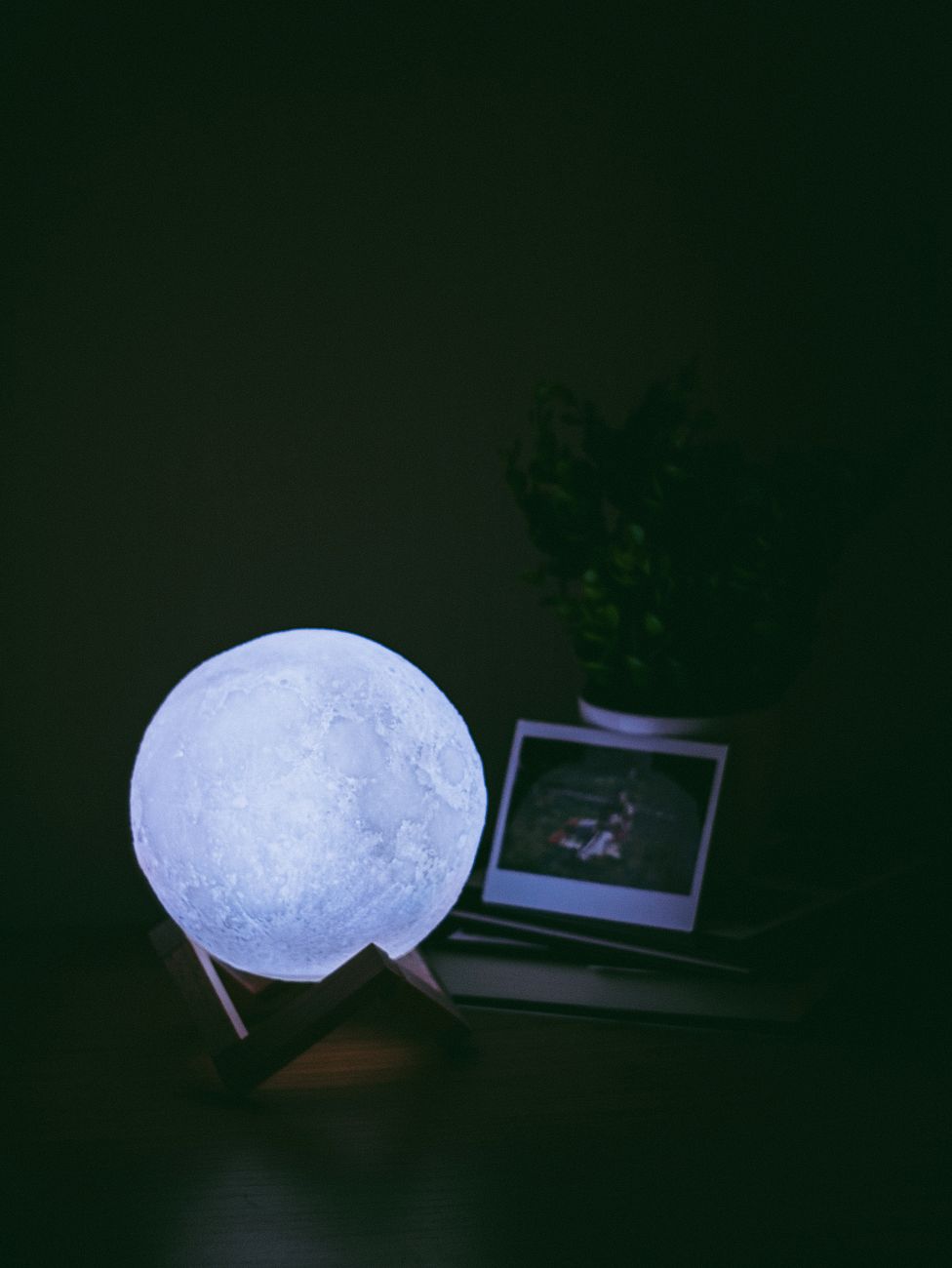A glowing moon lamp on a wooden stand provides ambient light in a dark room setting.