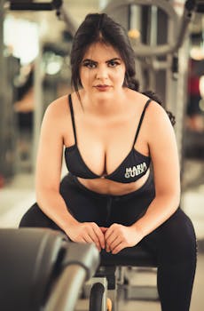 Confident woman in workout attire sitting on a bench in a gym setting.
