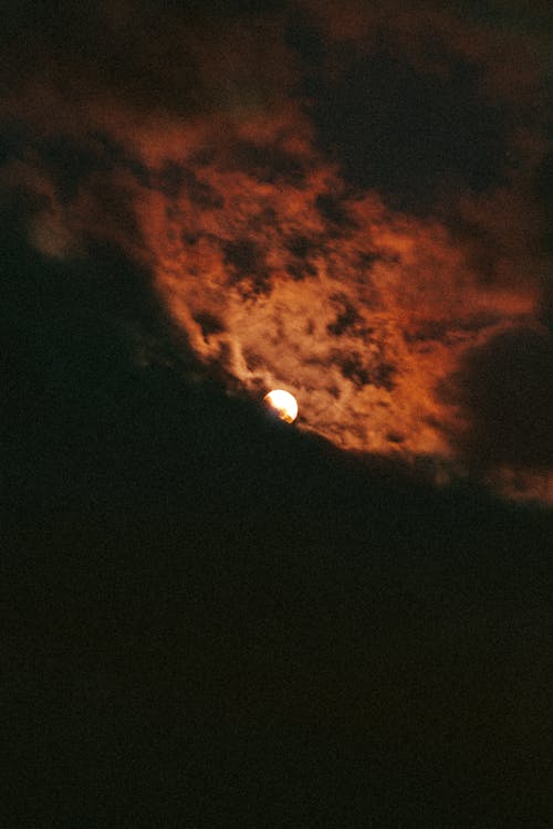Free Dramatic bright glowing moon in black sky surrounded by orange clouds late at night Stock Photo