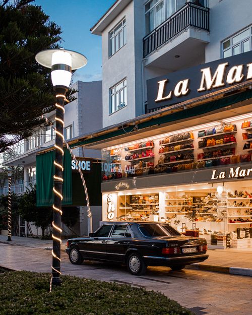 Free A vintage black Mercedes-Benz parked in front of a well-lit La Marca shoe store in Turkey at dusk. Stock Photo