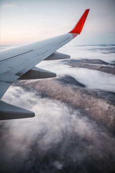 Scenic flight over mountains with view of airplane wing and clouds.