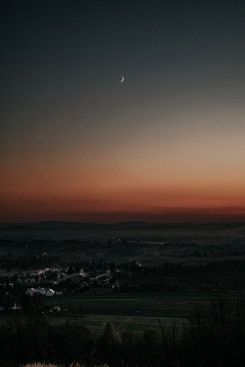 Free Quiet Polish village landscape at twilight under a crescent moon in a serene sky. Stock Photo
