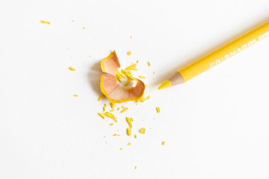 Top view of bright pencil with pointed shaft near dry wavy shavings and tiny fragile parts on white surface