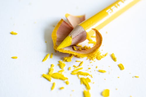 Sharpened bright yellow pencil with shavings on white surface
