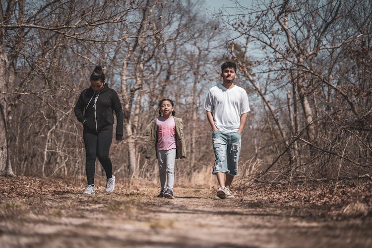 Ethnic Family Walking On Footpath Between Dry Trees In Countryside