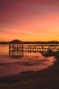 Spectacular view of coast and wooden pavilion on sea pier with fence behind mountains under colorful sky at sundown in twilight