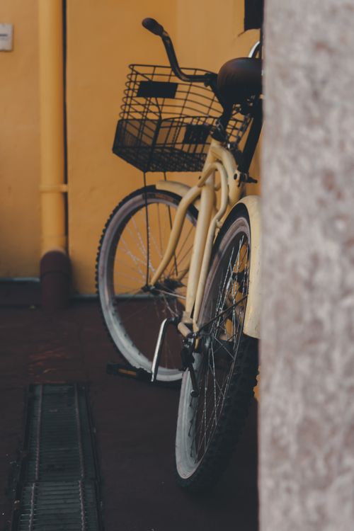 Free A classic vintage bicycle with a basket is parked against a vibrant yellow wall, capturing a rustic charm. Stock Photo