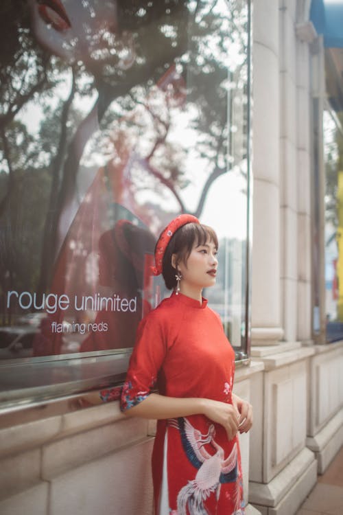 Woman in Red Dress Standing Beside Glass Window