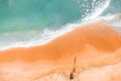 Free Drone view of colorful glowing sea water with foam on sandy coast with shadow of unrecognizable travelers in summer in sunlight Stock Photo