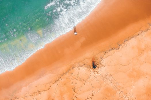 Drone view of bright sandy coast with stains on surface near pure foamy ocean water with ripples glowing in daylight