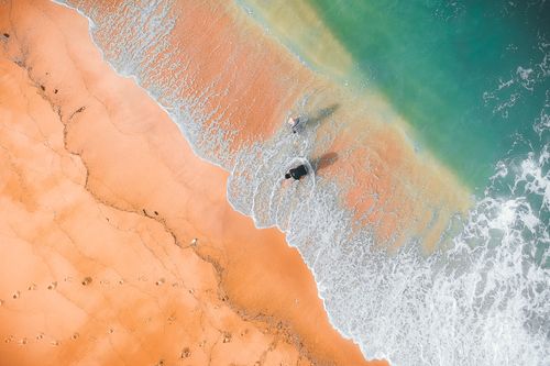 Free Aerial view of colorful sandy beach with wavy line and unrecognizable travelers standing near foamy sea water in summer during trip Stock Photo