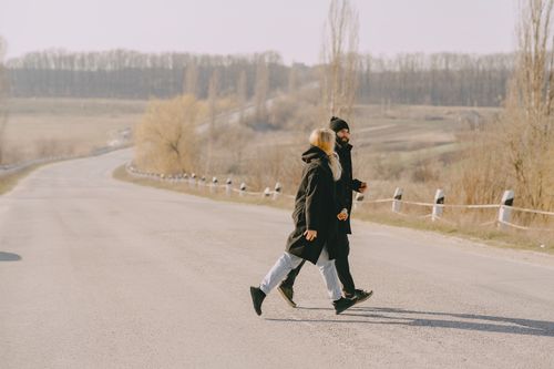 Free Careless male and female pedestrians wearing warm outerwear breaking rules of road safety running across narrow asphalt road without crosswalk during cold season in rural area Stock Photo