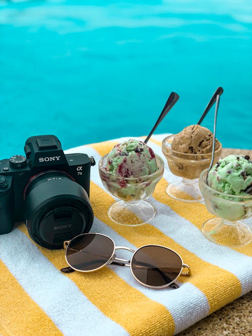 Ice Cream on Clear Glass Cups Beside A Sunglasses  and Black Sony Camera