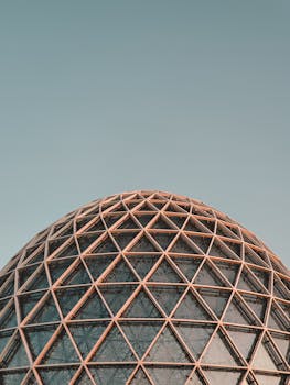 A modern spherical structure with geometric patterns beneath a clear blue sky.