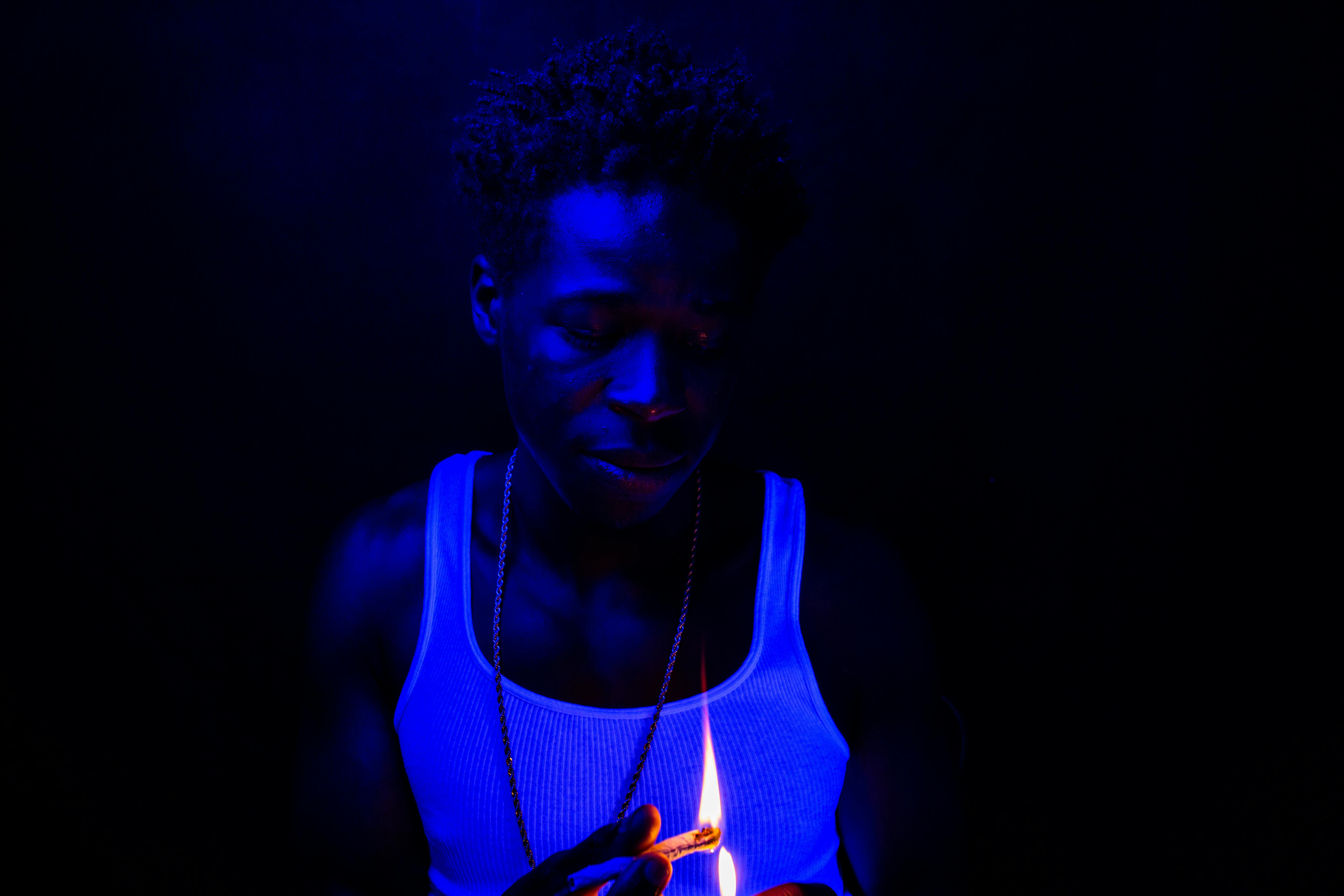 man in white tank top lighting a cigarette