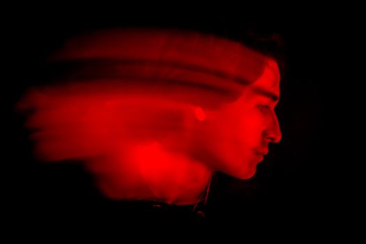 A captivating portrait of a man with motion blur, creating a dramatic red light effect against a black background.