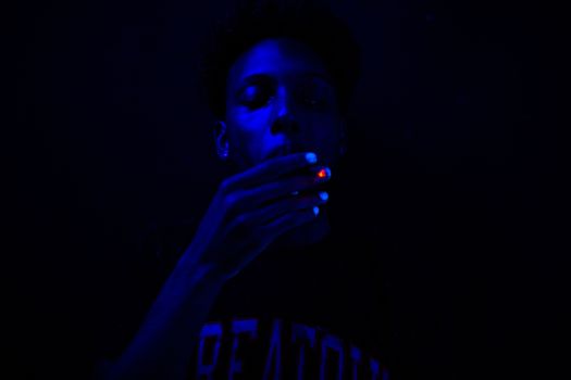 Close-up of a man smoking under blue ultraviolet lighting, creating a dramatic effect.