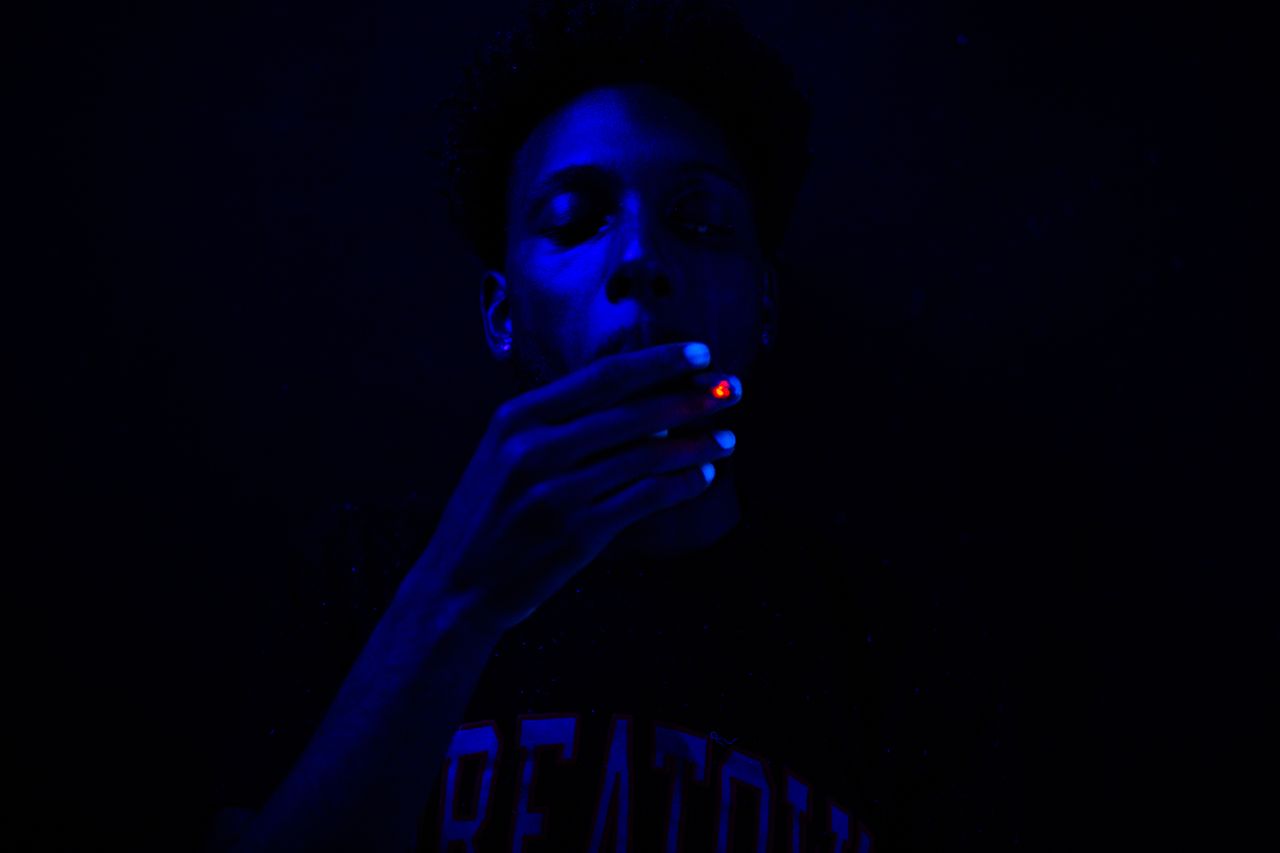close up of a man smoking under blue ultraviolet lighting creating a d