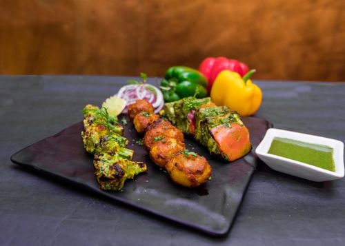 Free From above of delicious roasted broccoli with various colorful vegetables near onion slices and peppers on plate near bowl with spicy green salsa in cafe Stock Photo