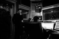 Black and white of unrecognizable sound man working on desktop computer using musical software while sitting in chair near pensive colleagues in recording studio