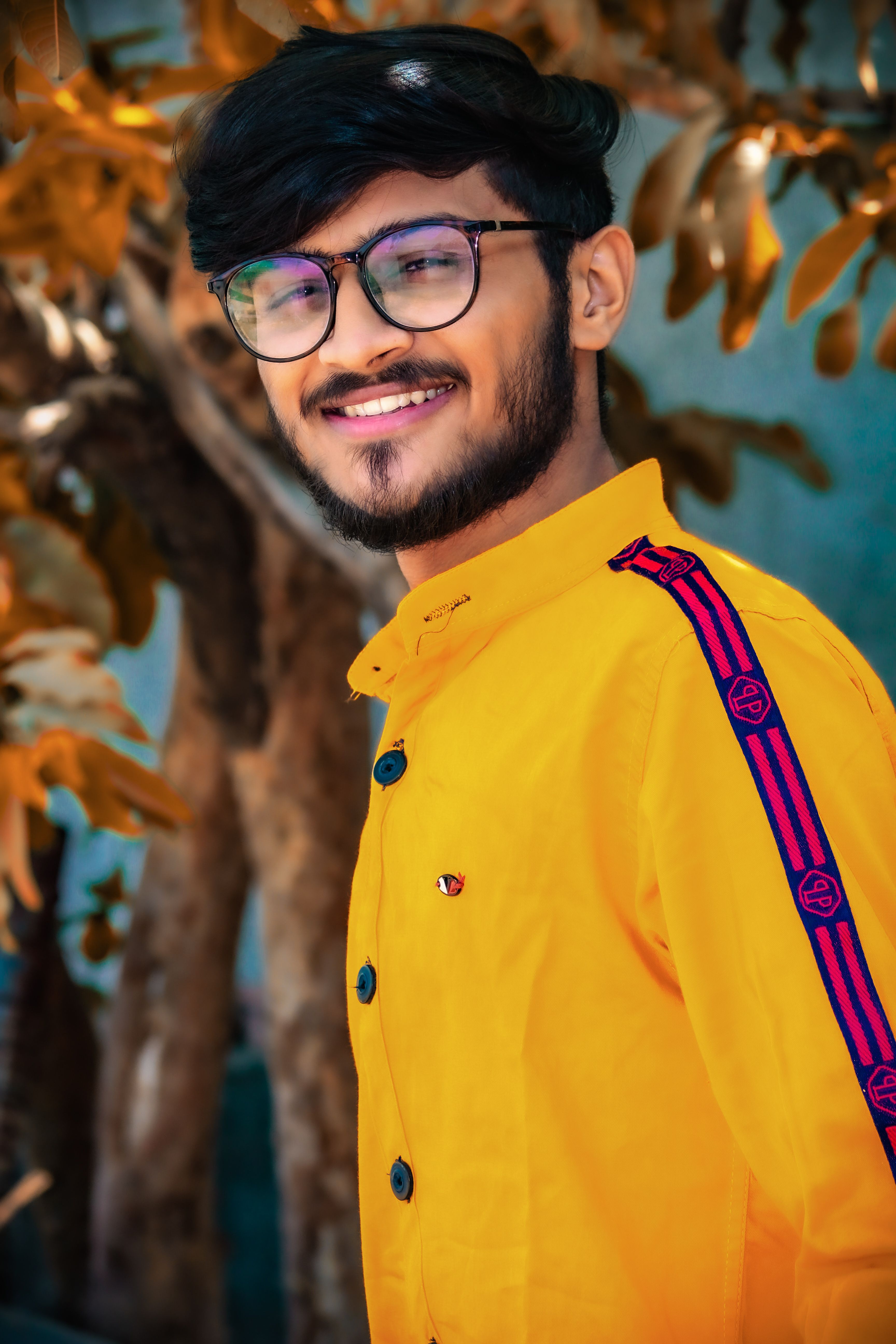 A smiling young man in a fashionable yellow outfit poses confidently outdoors, exuding style and warmth.