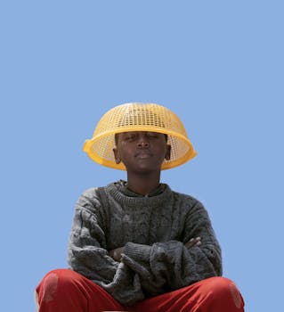 在简单的蓝色背景下，小男孩戴着塑料过滤器当帽子，拥抱创造力