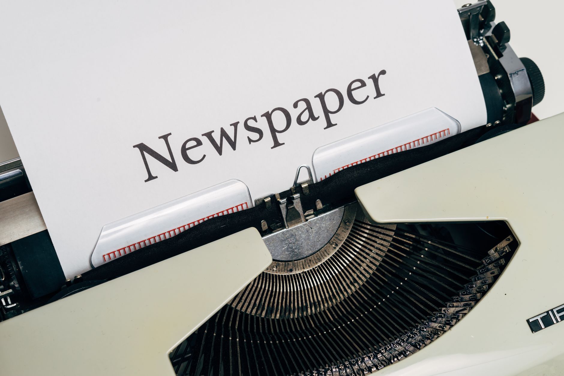 Close-up of a vintage typewriter printing the word 'Newspaper' on paper.