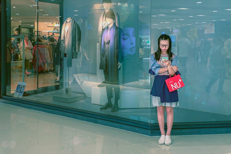 Focused Young Asian Woman Surfing Smartphone In Shopping Mall