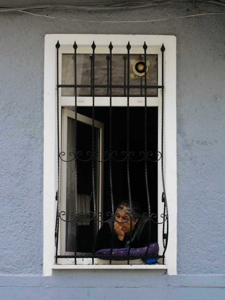 Thoughtful Senior Hispanic Woman Leaning On Hand On Windowsill